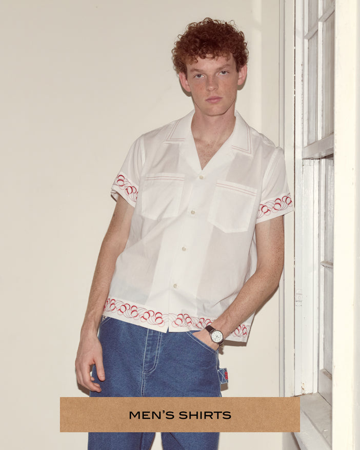 Model wearing a white shirt patterned with embroidered detail on the hem.