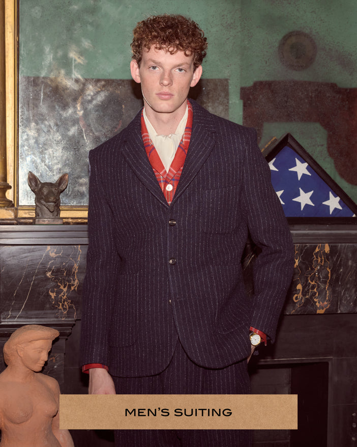 Model wearing a navy blue chalk stripe suit in front of a mantle.