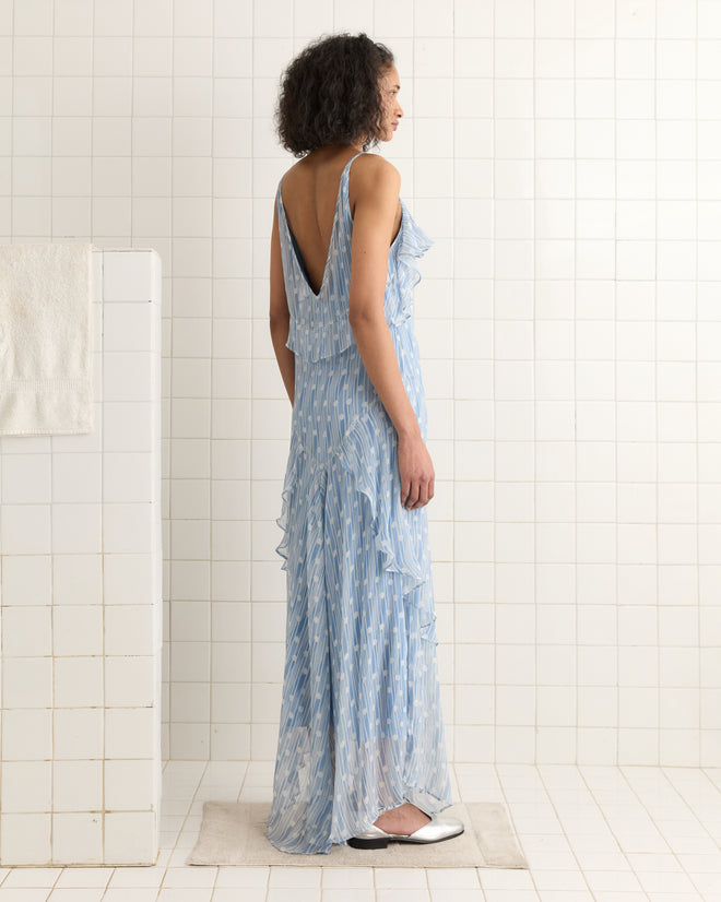 A person in the Meridian Gown, featuring an Art Deco design, stands on a white-tiled floor near a wall, viewed from the side.