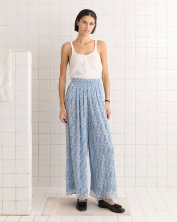 A woman in a white tank top and Meridian Pants stands gracefully in a tiled room.