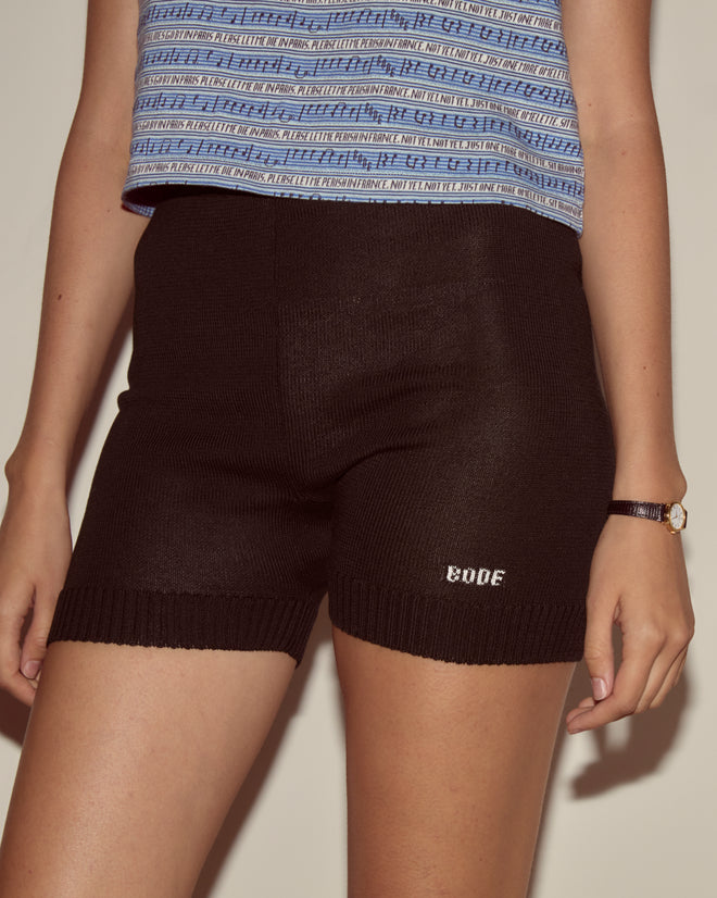 Person wearing a blue patterned top, Meringue Shorts - Black by Bode, and a wristwatch.