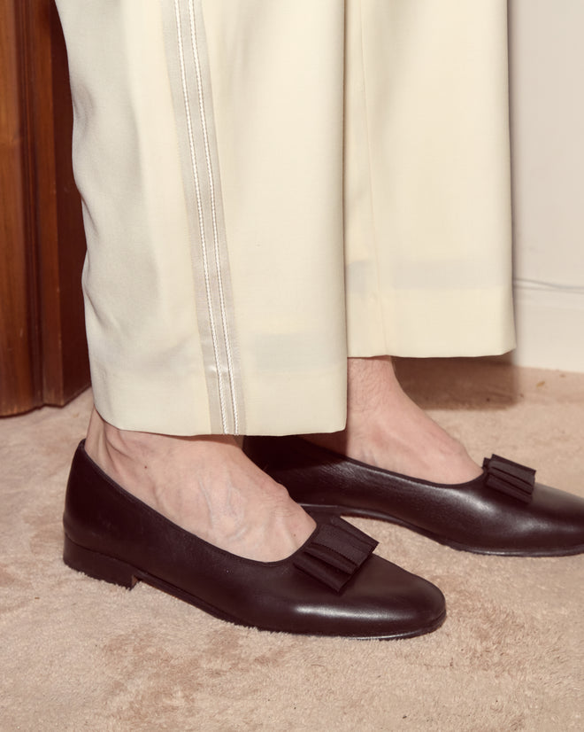 Person wearing Meringue Smoking Trousers in ivory wool and black loafers with bows, standing on a beige carpet.