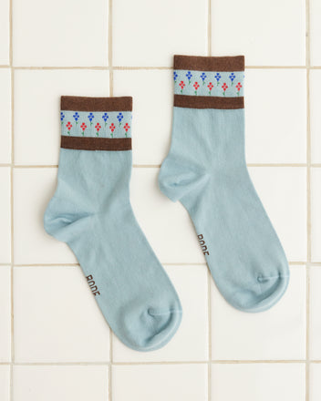 A pair of Bluebell Socks featuring a delightful floral pattern and brown cuffs, showcased on a white tiled floor.