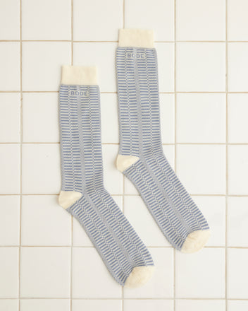 The Micro Check Socks in blue and cream, featuring intricate patterns with cream cuffs, toes, and heels, are artfully displayed on a tiled surface, highlighting the timeless appeal of vintage children's accessories.