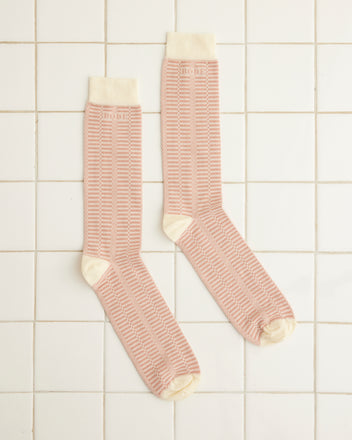 On a white tiled floor lay two Micro Check Socks in pink and cream, featuring a delightful vintage design. Crafted in Italy, these children's cotton socks bring a touch of European charm to any space.