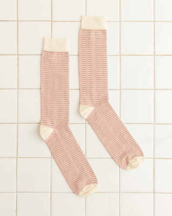 A pair of Micro Check Socks in pink and cream, featuring a retro pattern and cream toes, heels, and cuffs, rest on a white tiled surface.