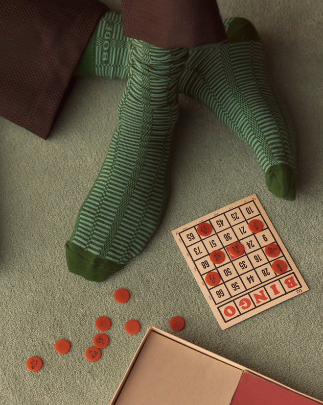 A person wearing Micro Check Socks - Green is playing bingo on a green carpet, clutching a bingo card and chips.