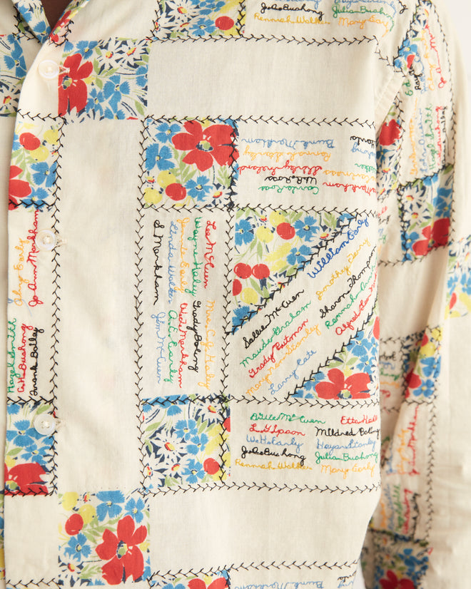 Close-up of the White Micro Signature Long Sleeve Shirt showcasing colorful floral patterns and embroidered text patches, bordered with black stitching on a cream background, reminiscent of antique patchwork.