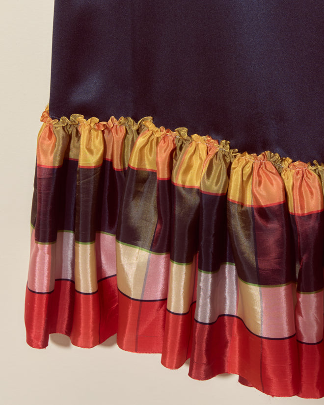 A close-up of the Midnight Gala Dress - Navy showcases its shiny silk satin fabric and ruffled, multicolored striped hem inspired by vintage ribbon, set against a plain background for a unique look.