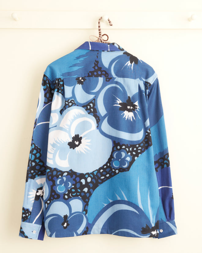 The Mink Protea Long Sleeve Shirt in size S/M, known for its unique swirling blue floral pattern, is hanging on a white wall.