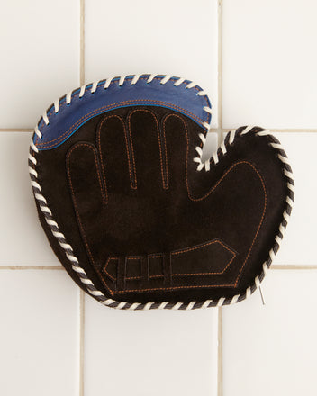 The Mitt Clutch, featuring a sleek black and blue design with white stitching, elegantly rests on a white tiled surface, adding a touch of sophistication to any sports enthusiast's collection.