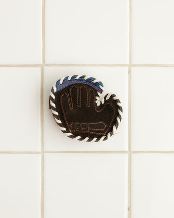 A Mitt Coin Purse rests on a white tiled surface, reminiscent of classic leather accessories.