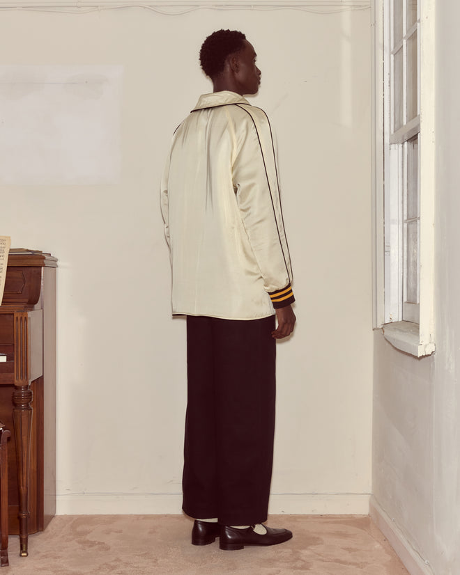 A person in a Monogram Snap Reversible Jacket and black pants stands facing a corner in a sparsely furnished room.