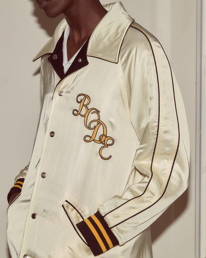 A person wearing the Monogram Snap Reversible Jacket, a shiny cream jacket with black stripes and a chain-stitched 