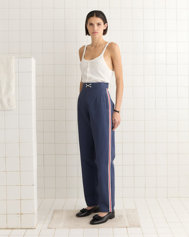 In a tiled room, someone wears a white tank top and Monterrey Stripe Trousers in heavyweight blue twill with a drawstring waist.