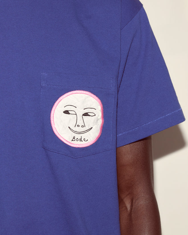 The Moon Tee is a blue cotton t-shirt with a pocket, featuring a smiling face patch and "Bode" embroidered underneath.