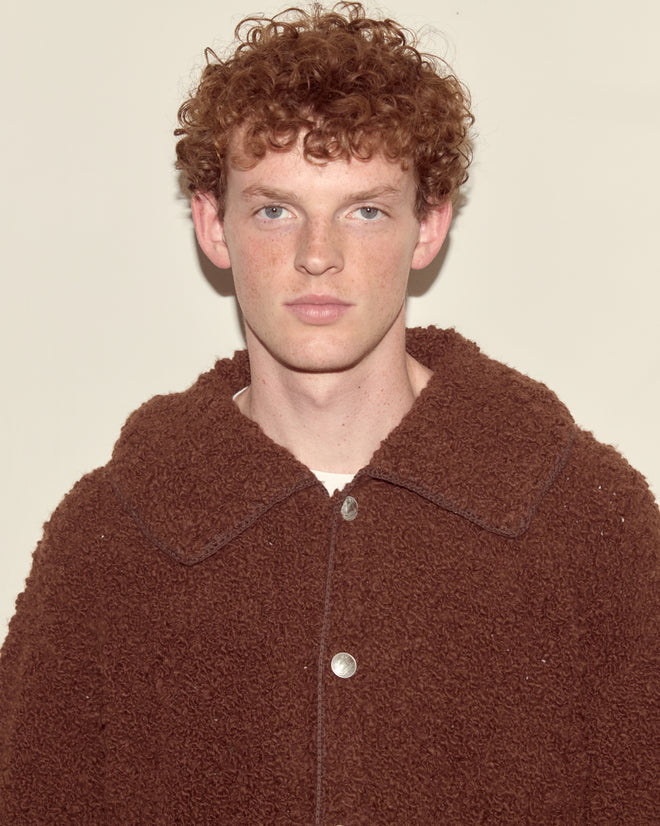 A person with curly red hair wears the oversized Moppet Cardigan in brown, standing against a plain light background.