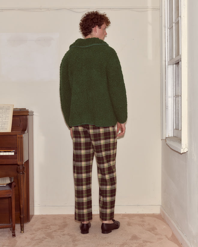 Wearing the Moppet Cardigan - Green and plaid pants, a person stands facing the corner of a room near a piano and window.