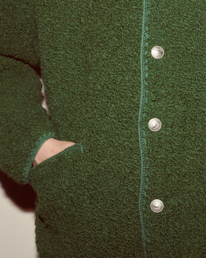 Person wearing the Moppet Cardigan in green, featuring bouclé yarn, silver buttons, an oversized silhouette, and a hand in its pocket.