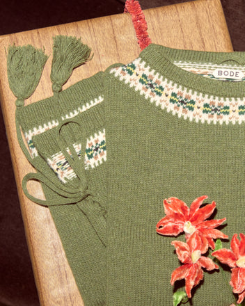 The Moritz Sweater: a green virgin wool knit with floral embroidery, tassels, and a patterned collar, folded neatly on a wooden surface—luxury knitwear redefined.