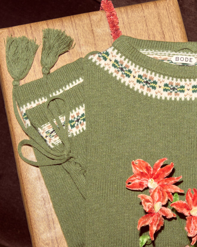 The Moritz Sweater: a green virgin wool knit with floral embroidery, tassels, and a patterned collar, folded neatly on a wooden surface—luxury knitwear redefined.