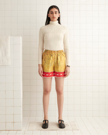 In a tiled room, someone confidently faces forward, donning a Morocco Map Shorts with colorful detailing. The elastic waistband adds comfort to their outfit, creating a striking contrast against the room's backdrop.