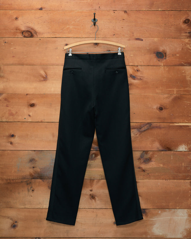 Tropical Wool Double-Button Trousers hanging on a wooden hanger against a wooden plank wall background.