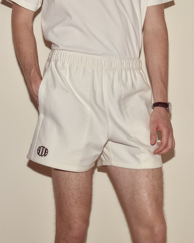 Person wearing a white t-shirt and Field Shorts - White, crafted from heavyweight cotton twill, hands in pockets with the Bode logo subtly visible, standing against a plain background.