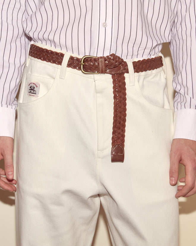 Person wearing a striped shirt, Twill Knolly Brook Trousers - White, and a braided brown belt with the end hanging down.