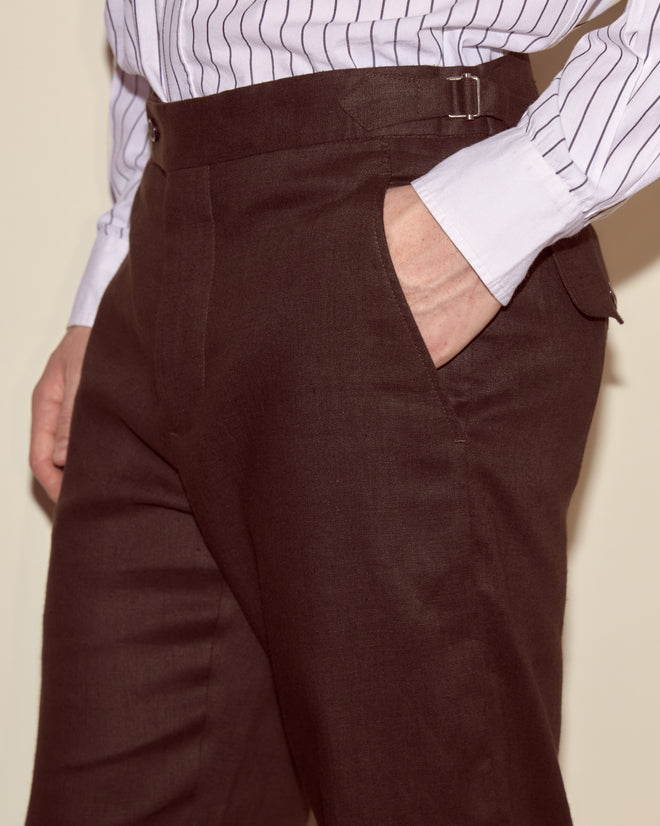 Person wearing Lightweight Linen Side-Buckle Trousers in brown with a white striped shirt, hand in pocket.