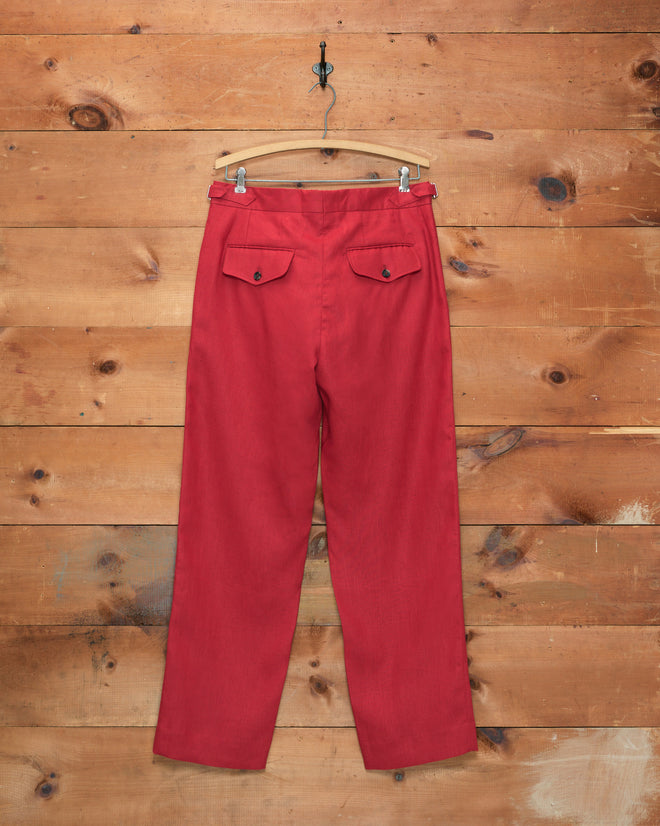 Lightweight Linen Side-Buckle Trousers - Red for men with flap back pockets hang on a wooden hanger against a rustic wooden wall background.
