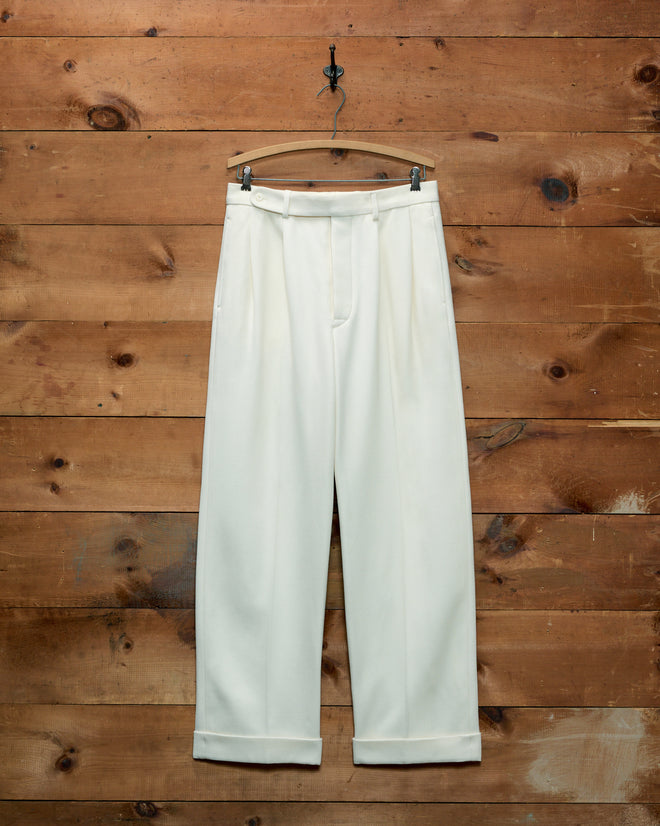 Off-white wool twill Riding McNab Trousers with pleated fronts and cuffed hems hanging on a wooden hanger.