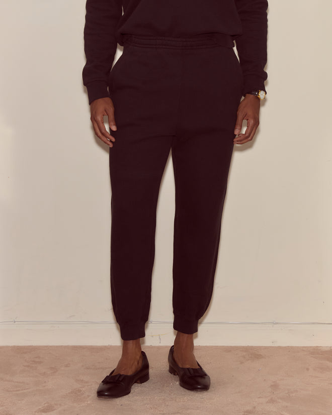 A person wearing Joggers - Black stands against a plain light-colored wall, paired with black loafers.