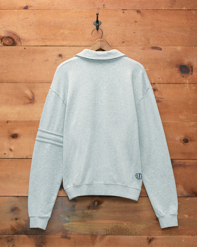 Heathered grey Crew Polo made from 100% cotton, displayed hanging on a hook against a wooden wall, shown from the back.