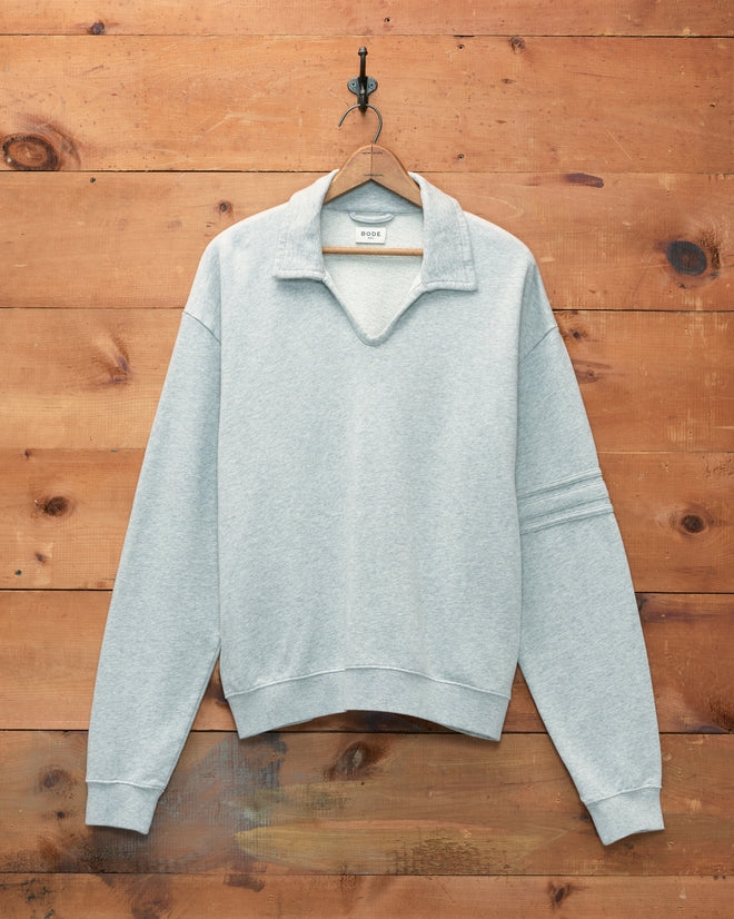 Heathered Grey Crew Polo, made from 100% cotton, featuring a collared pullover design and displayed against a wooden wall background.