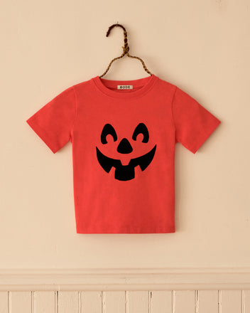 Pumpkin Kids’ Tee featuring a red short-sleeved shirt with a black jack-o’-lantern face print.