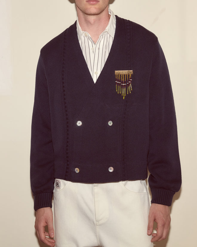 A man facing forward wears a Double-Breasted Cardigan in navy, paired with a striped shirt and white pants.