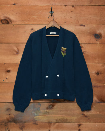 Double-Breasted Cardigan - Navy, featuring white buttons and a yellow hand-embroidered patch, displayed against a wooden wall.