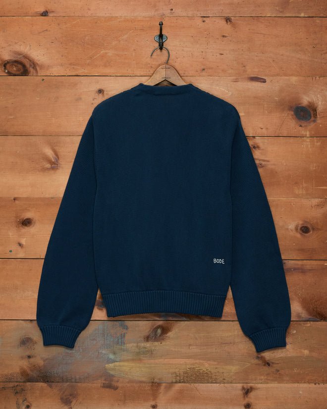 Double-Breasted Cardigan - Navy, featuring ribbed cuffs and hem and a small “BODE” logo, hangs against a wooden backdrop—this classic knitwear piece brings subtle sophistication to your wardrobe.