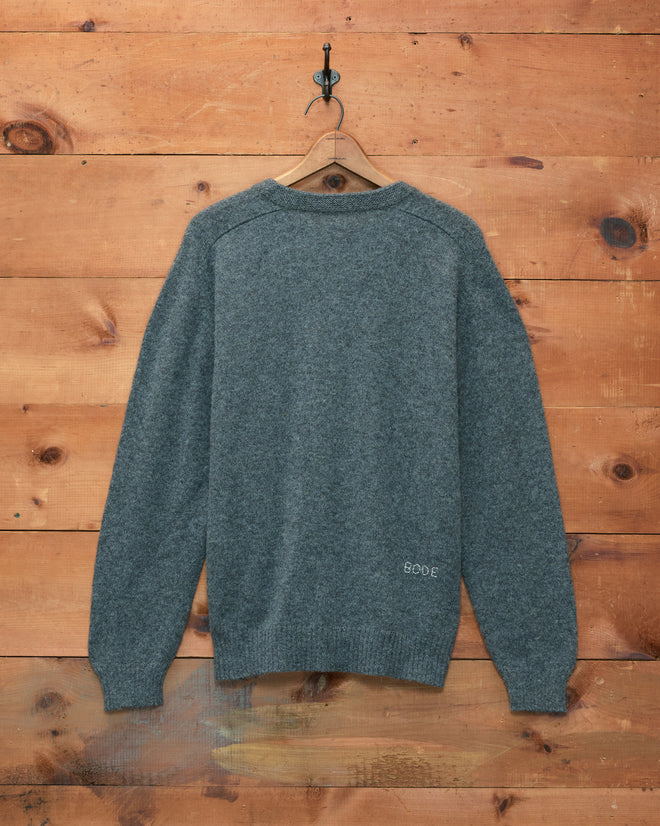 Orchard Cardigan - Grey hanging on a wooden wall, viewed from the back with a “BODE” label on the bottom hem, reminiscent of a classic merino wool cardigan.