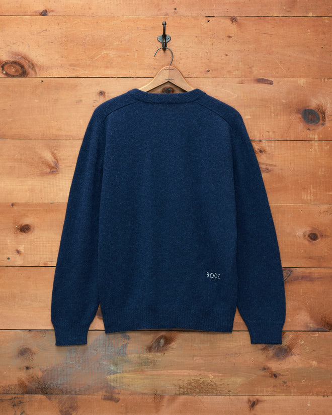 Orchard Cardigan - Navy, a long-sleeve merino wool piece, hanging on a hook and displayed against a wood plank wall.