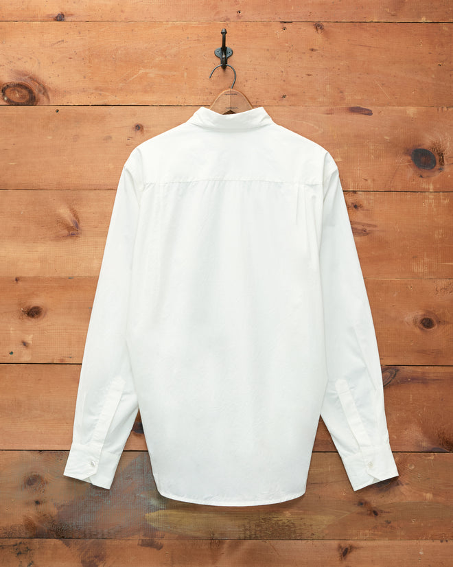 A white long-sleeve Monogrammed Poplin Shirt from the 1930s, displayed from the back on a hook against a wooden wall, features an elegantly embroidered Bode monogram.