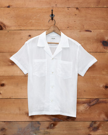 Voile Short Sleeve Shirt - White, featuring a boxy silhouette, two chest pockets, and short sleeves, crafted from white cotton voile; displayed on a wooden hanger against a wooden wall.