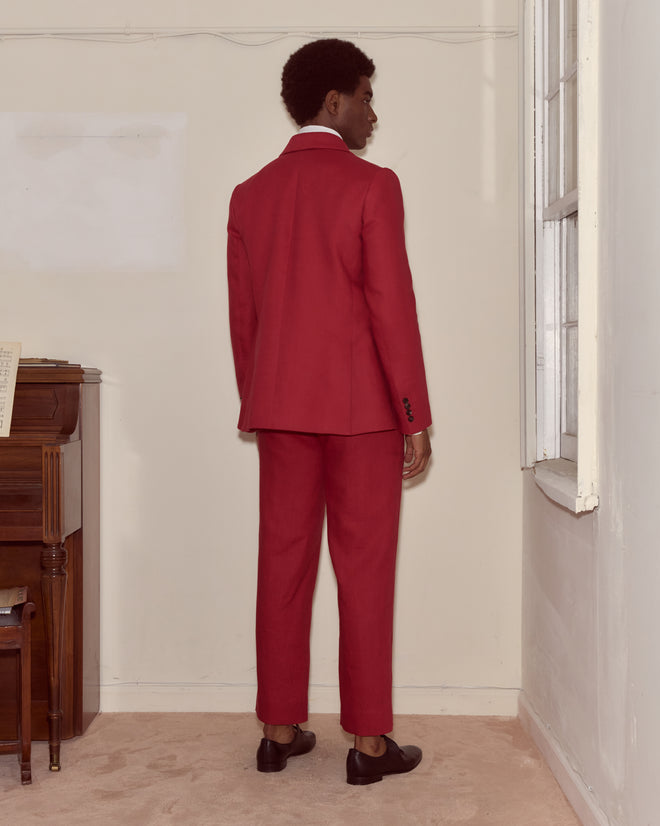 A person wears the Lightweight Linen Double-Breasted Suit Jacket - Red, standing near a piano and window in a minimal room, capturing spring summer minimalism.