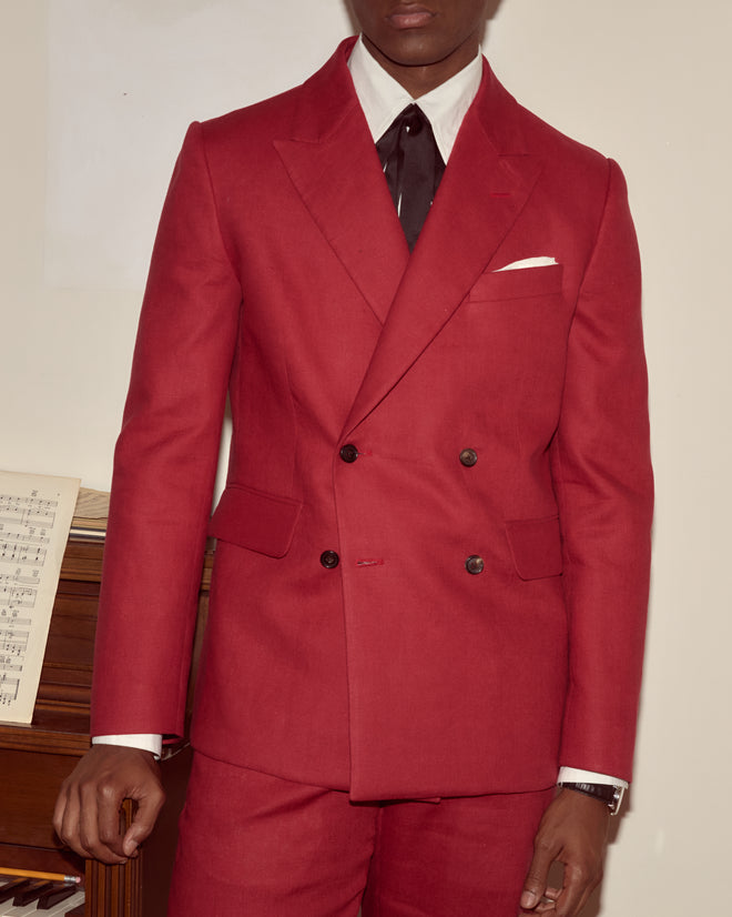 A person wearing the Lightweight Linen Double-Breasted Suit Jacket - Red, styled with a white pocket square and dark tie—perfect for spring and summer occasions indoors.