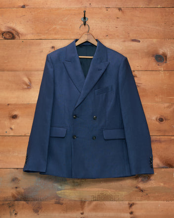 Lightweight Linen Double-Breasted Suit Jacket in Midnight hanging on a wooden wall with a black hanger—a perfect spring-summer blazer.