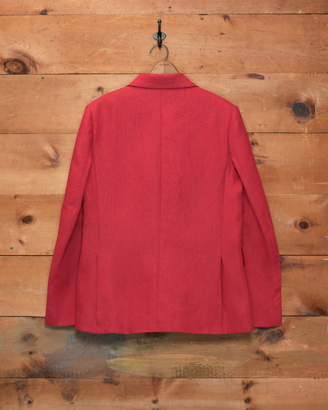 The Lightweight Linen Double-Breasted Suit Jacket in red hangs on a hook against a wooden wall, displayed from the back—an elegant nod to men’s spring-summer suiting.