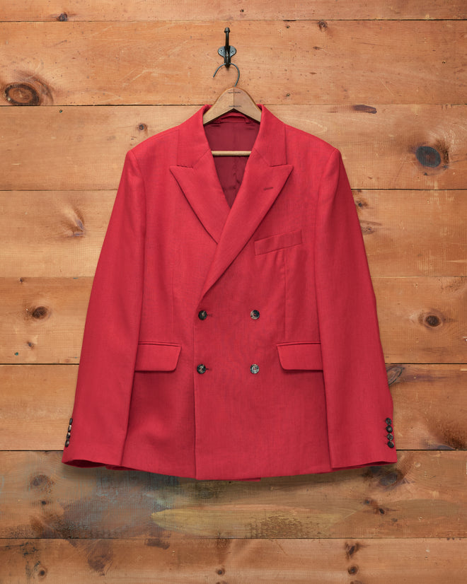 The Lightweight Linen Double-Breasted Suit Jacket - Red, ideal for men’s spring and summer suiting, is displayed on a wooden hanger against a rustic wooden wall.