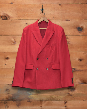 The Lightweight Linen Double-Breasted Suit Jacket - Red, ideal for men’s spring and summer suiting, is displayed on a wooden hanger against a rustic wooden wall.