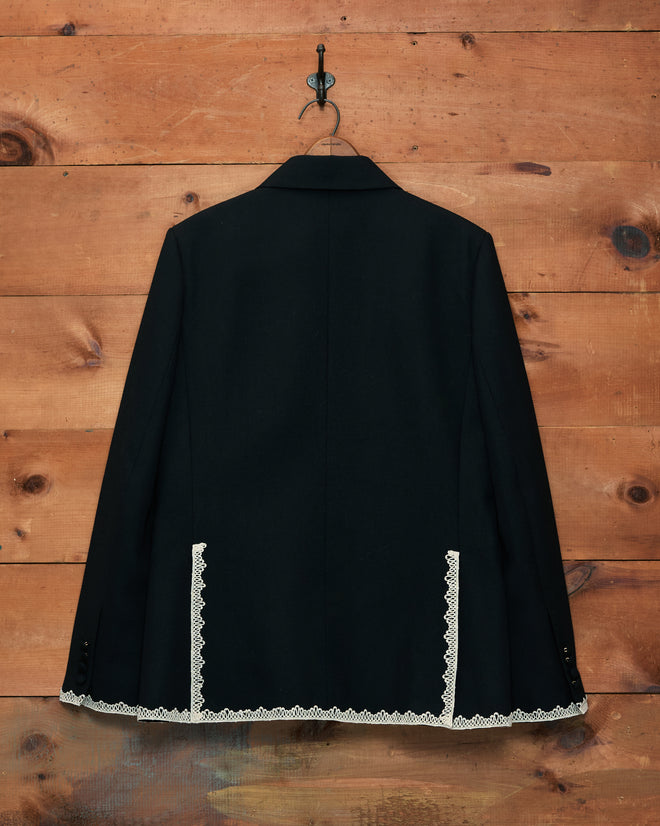 Lacework Double-Breasted Tuxedo Jacket featuring white machine lace trim on the lower back, inspired by classic midcentury styling, displayed hanging on a hook against a wooden wall.